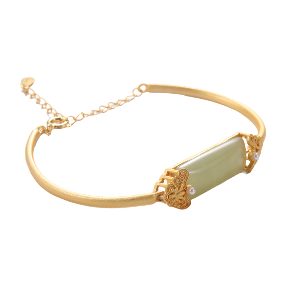Vintage inspired gold bangle with pale green gemstone, filigree, and pearl accents.