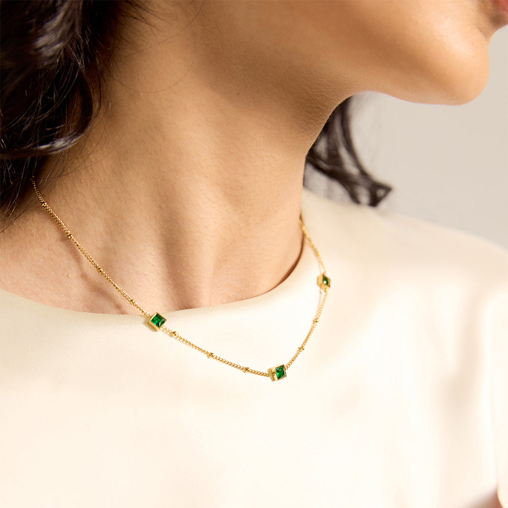 Close-up of woman wearing gold tone chain necklace with square green gemstones.