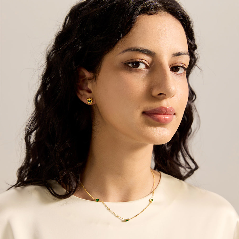 Model wearing gold chain necklace with square green gemstones, paired with matching earrings.