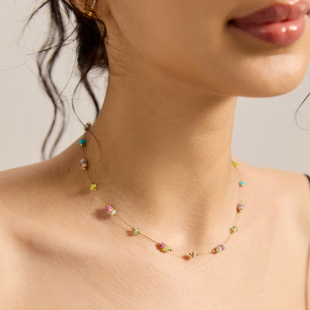 Close-up of woman wearing dainty gold chain necklace with multicolor pastel stone beads.