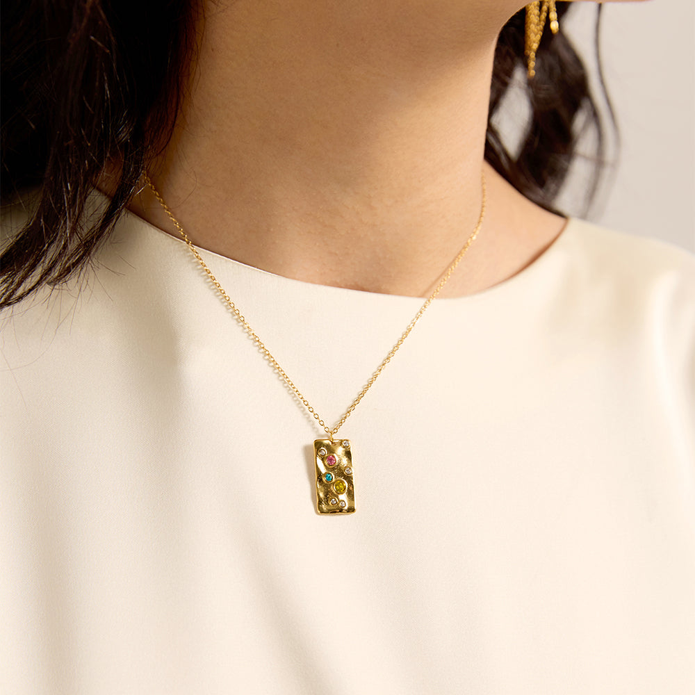 Close-up of woman wearing gold tone textured rectangle necklace with vibrant chakra crystals.