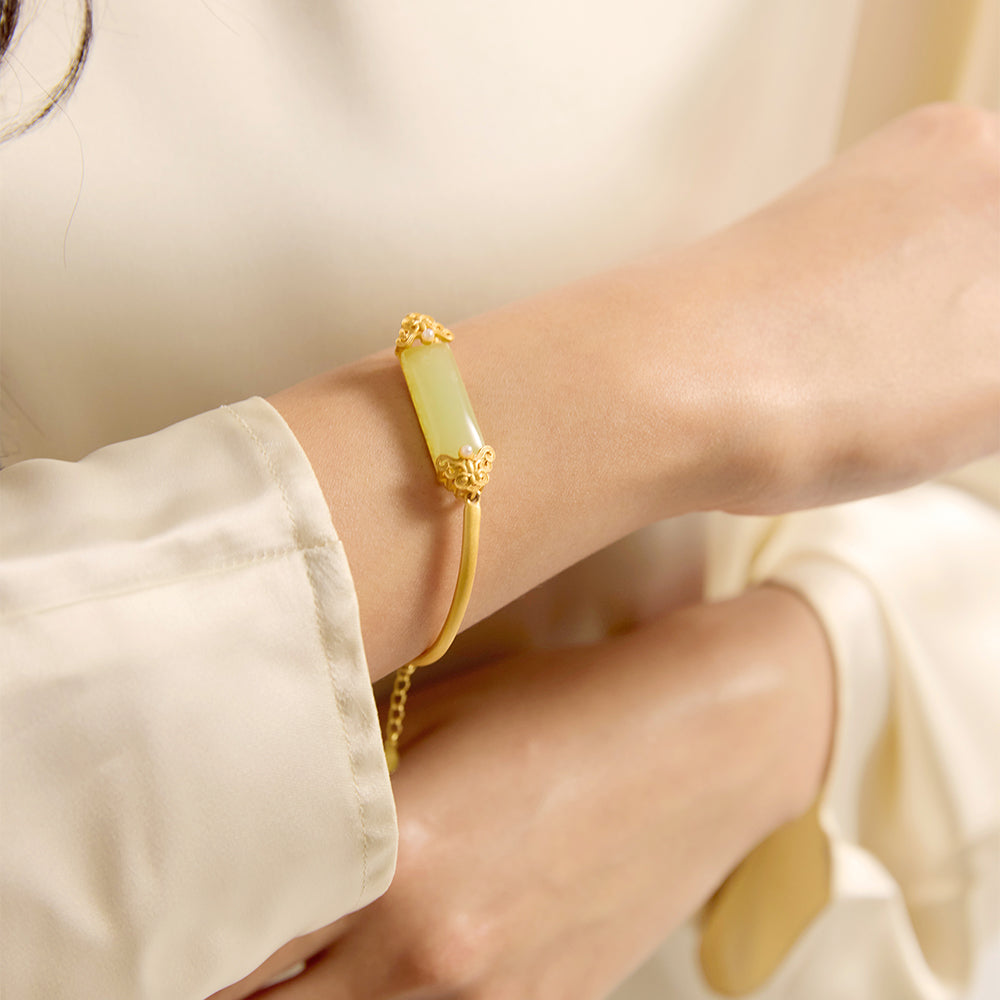 etailed view of gold bangle showing green gemstone, intricate filigree, and pearl accents.