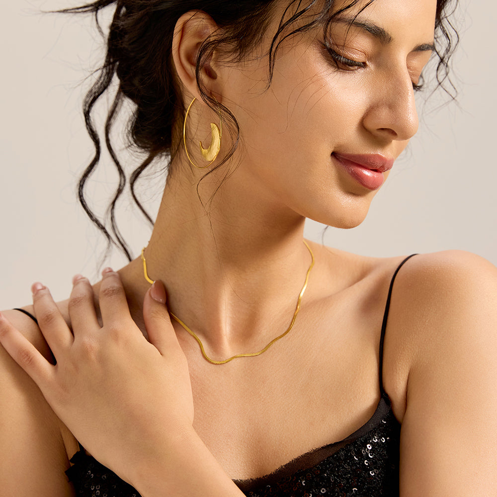 Close-up of woman wearing gold tone herringbone snake chain necklace, highlighting its sleek drape.
