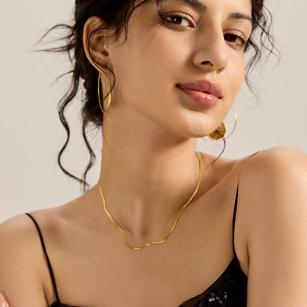 Model showcasing gold tone herringbone snake chain necklace, complementing an elegant outfit.