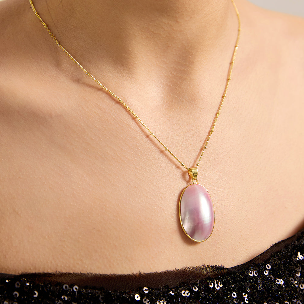 Close-up of woman wearing gold tone satellite chain necklace with iridescent oval pendant.