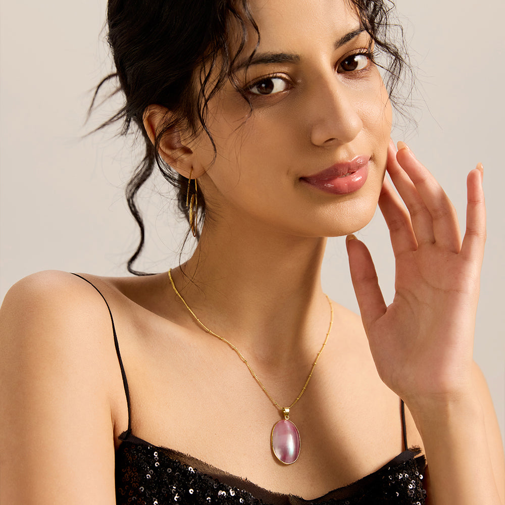 Model showcasing elegant gold tone satellite chain necklace with iridescent oval pendant, complementing a chic look.