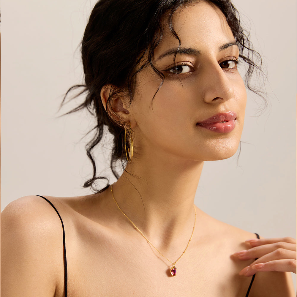 Model showcasing elegant gold tone satellite chain necklace with red gemstone, complementing a chic look.