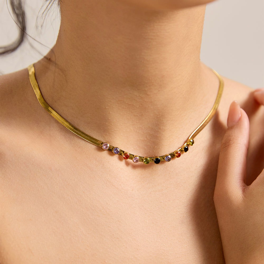 Model wearing gold snake chain necklace with multicolor gemstones, styled with matching earrings.