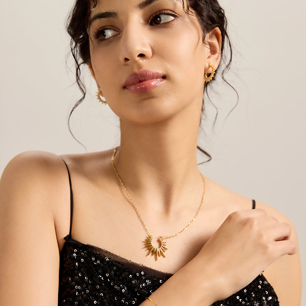Model wearing radiant gold tone sunburst pendant necklace, paired with matching earrings, completing a chic look.