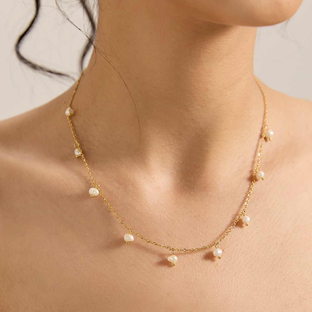 Close-up of woman wearing gold tone dainty chain necklace with freshwater pearls.