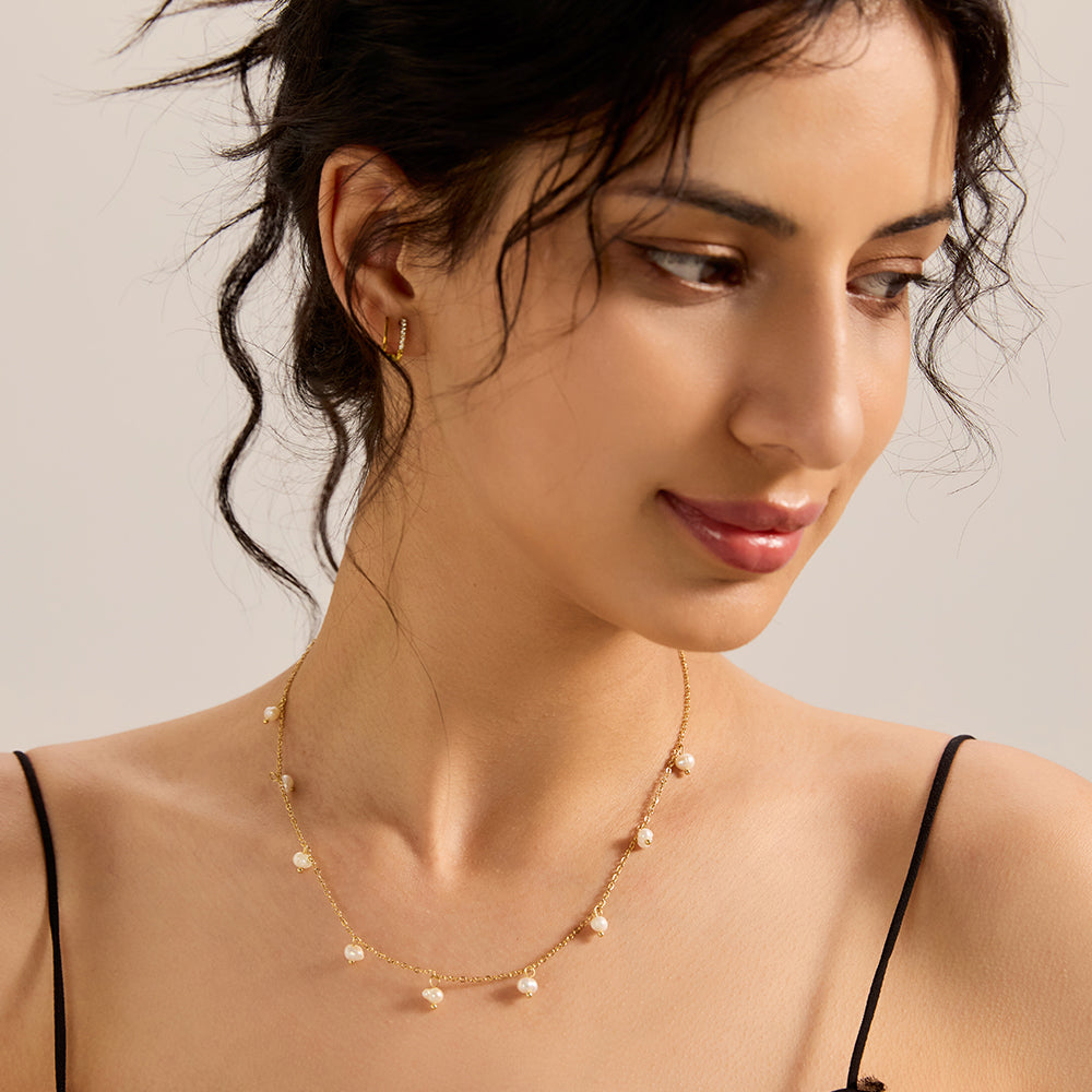 Model showcasing elegant gold tone dainty chain necklace with freshwater pearls, complementing a chic look.
