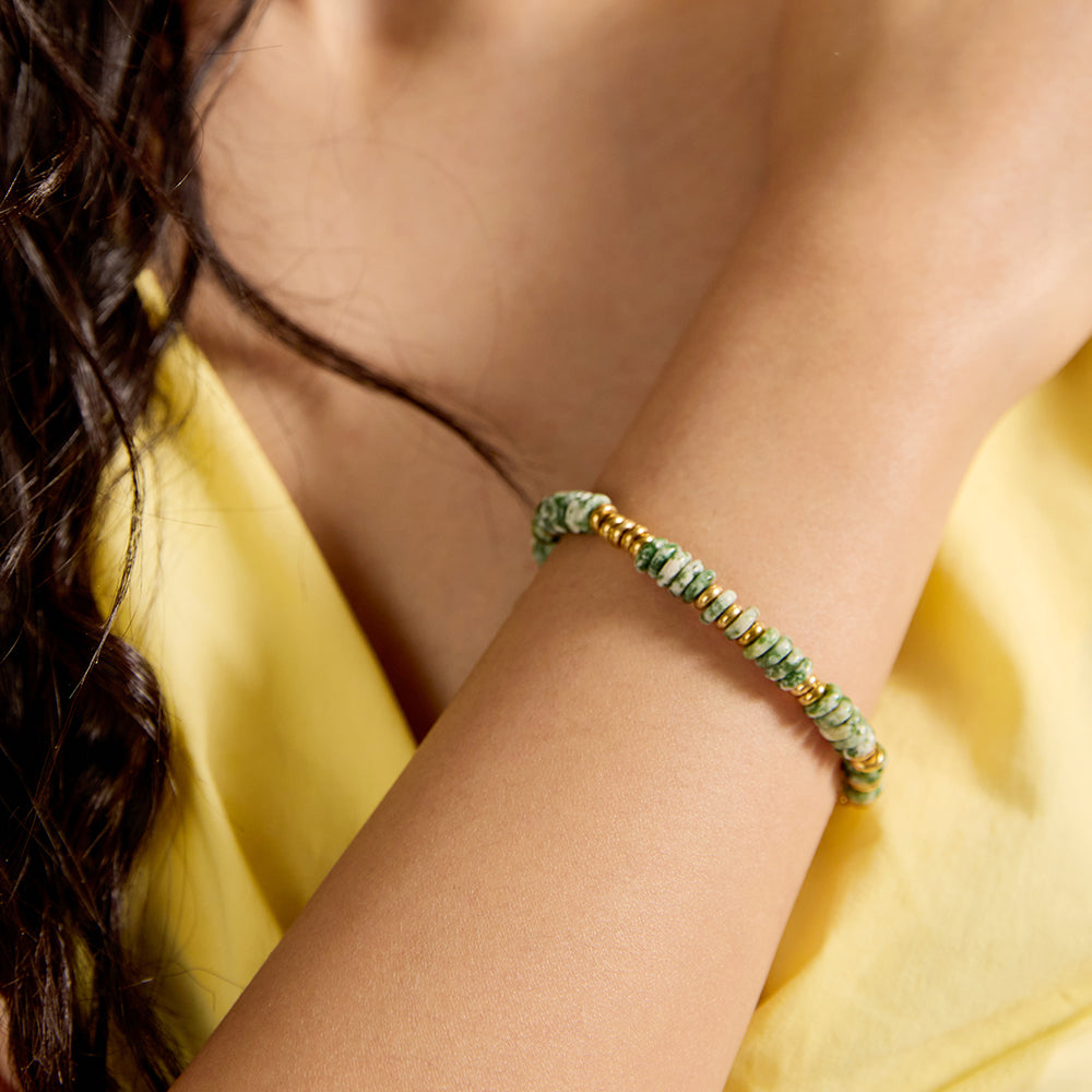 Close-up of woman's wrist wearing dainty green stone and gold bead bracelet.