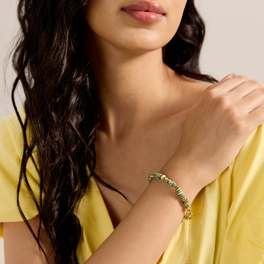 Woman's arm with green stone and gold bead bracelet, part of a chic everyday outfit.