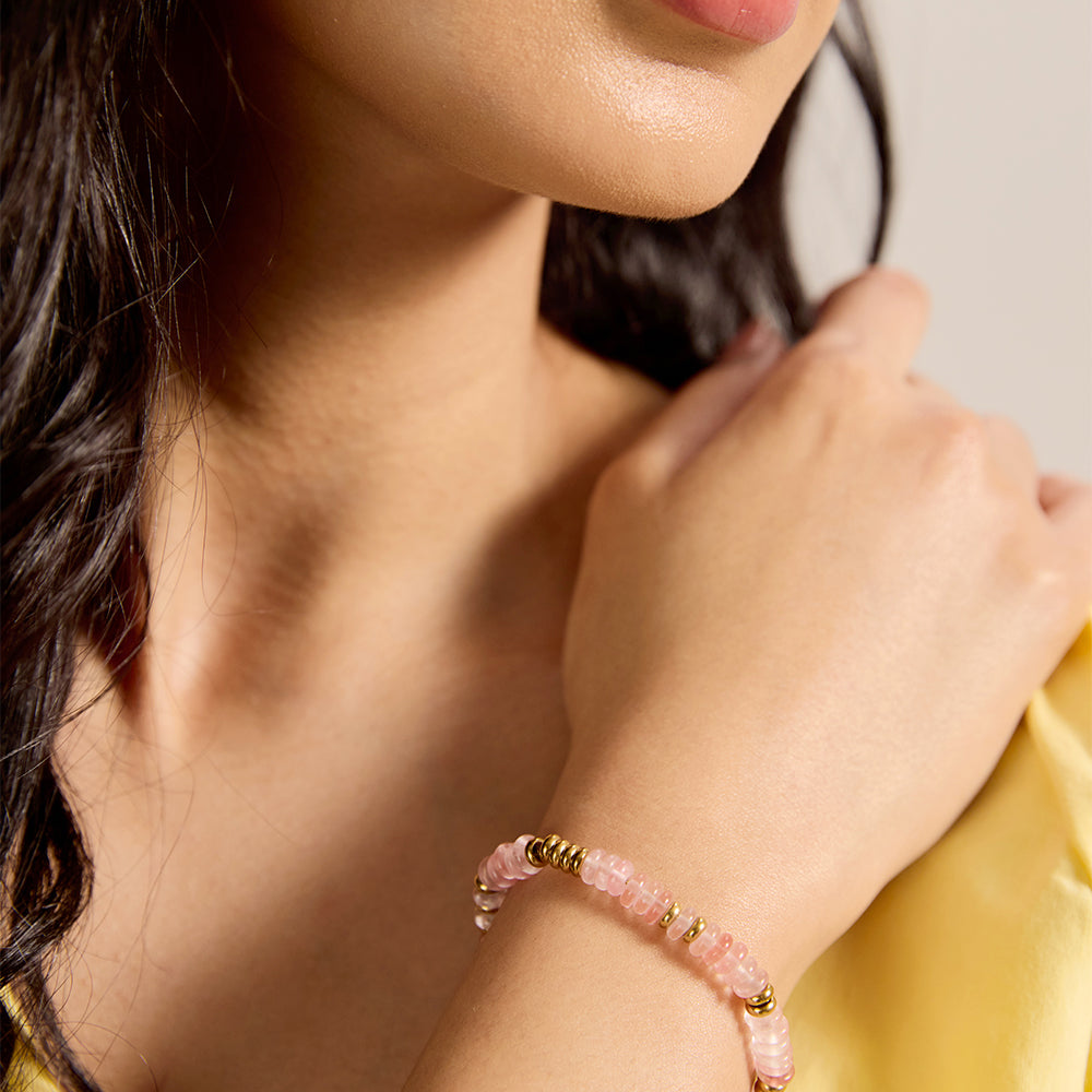 Close-up of woman's wrist wearing dainty pink stone and gold bead bracelet.