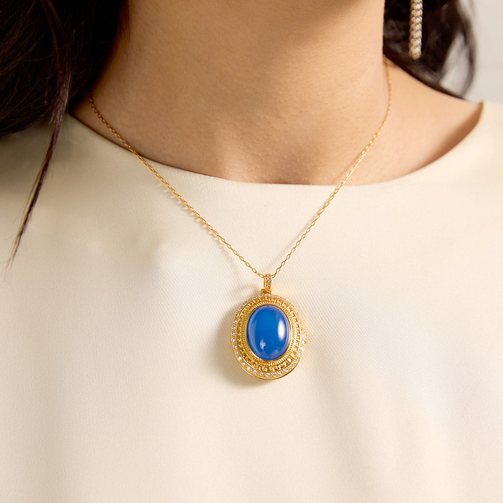 Close-up of woman wearing spiritual gold tone oval blue gemstone amulet necklace, highlighting its serene beauty.