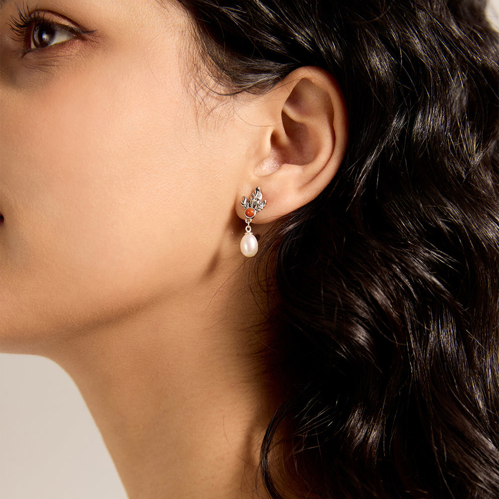 Close-up of woman wearing artisan sterling silver leaf and red gemstone pearl drop earring.