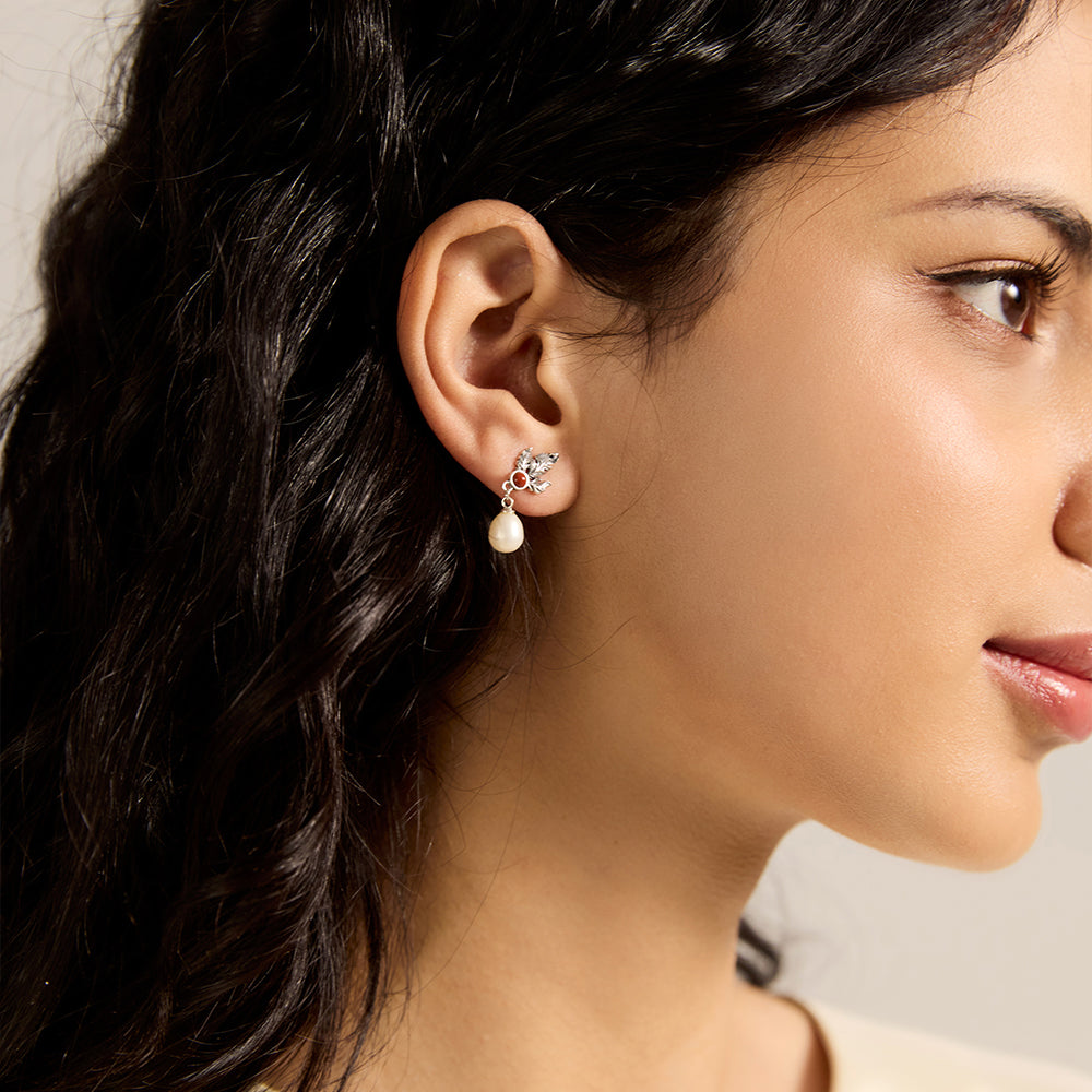Woman wearing elegant sterling silver leaf red gemstone and pearl drop earrings.