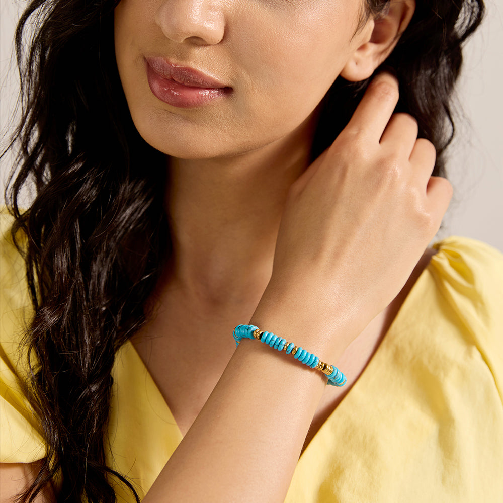 Close-up of woman's wrist wearing vibrant turquoise and gold bead bracelet.