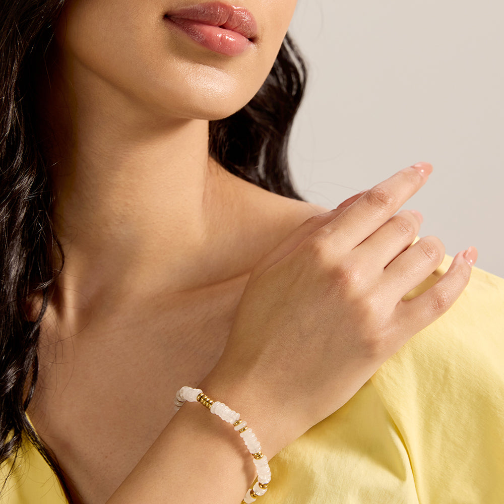 Close-up of woman's wrist wearing dainty white stone and gold bead bracelet, perfect for everyday style.